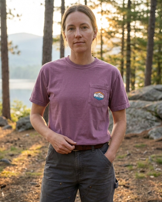 Person wearing a purple t-shirt with a logo in a forest setting