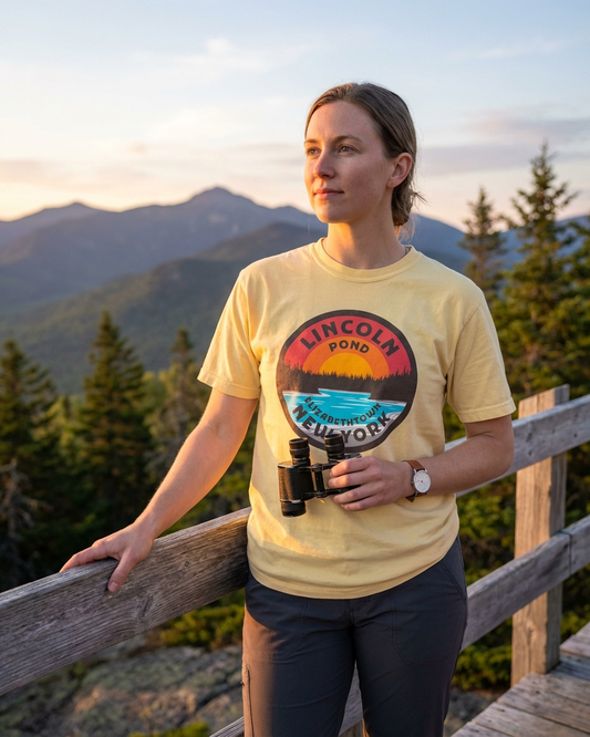 Woman wearing a yellow t-shirt with a scenic design, standing in a mountainous landscape.