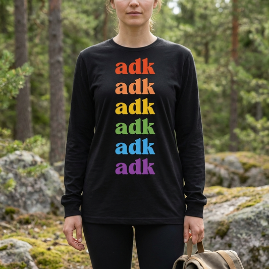 Person wearing a black long-sleeve shirt with 'adk' in rainbow colors standing in a forest.