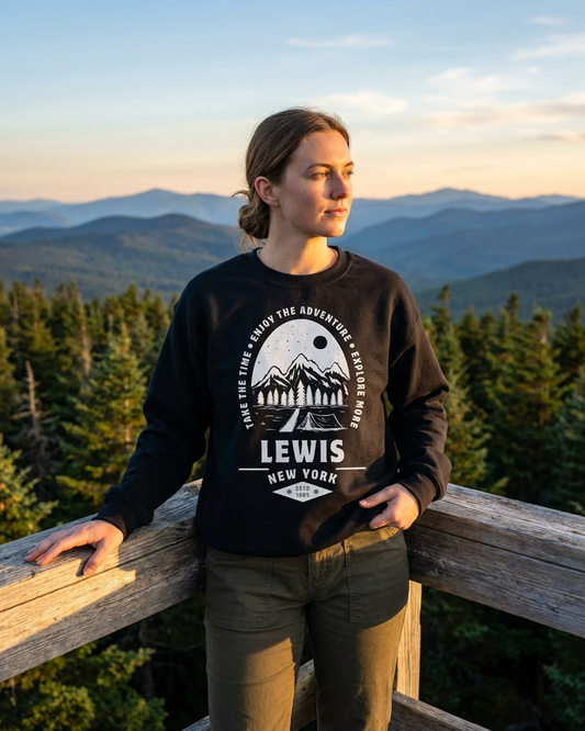 Person wearing a black sweatshirt with a mountain design and 'LEWIS NEW YORK' text, standing in front of a scenic mountain landscape.