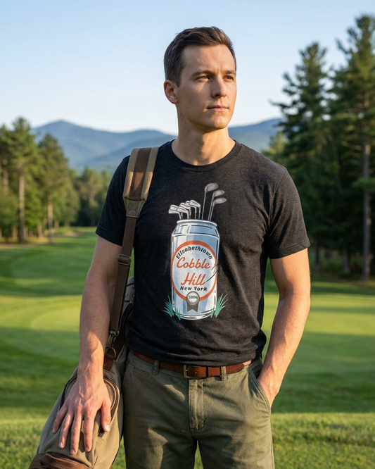 Man wearing a black t-shirt with a graphic design, standing on a golf course with trees and mountains in the background.