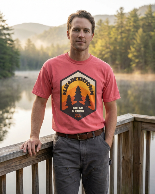 Man wearing a red Elizabethtown New York t-shirt with a nature-themed design, standing by a lake with trees and mountains in the background.