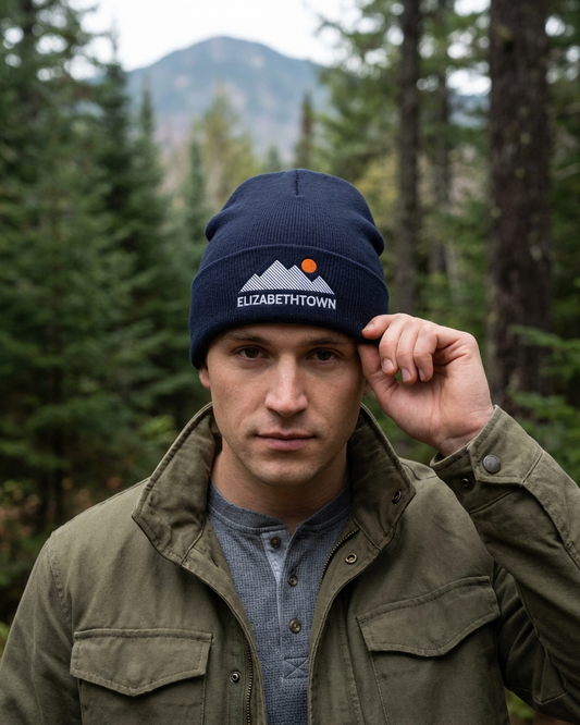 Man wearing a navy blue beanie with 'Elizabethtown' logo in a forest setting