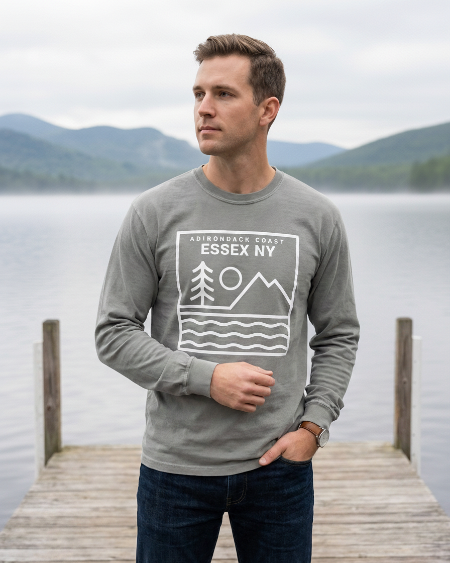 Man wearing a gray sweatshirt with 'Essex NY' design standing on a dock by a lake.