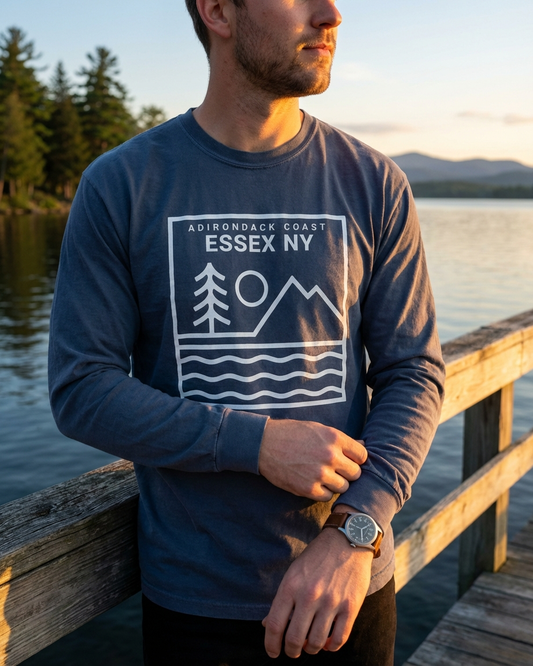 Person wearing a blue long-sleeve shirt with 'Essex NY' design by a lake.