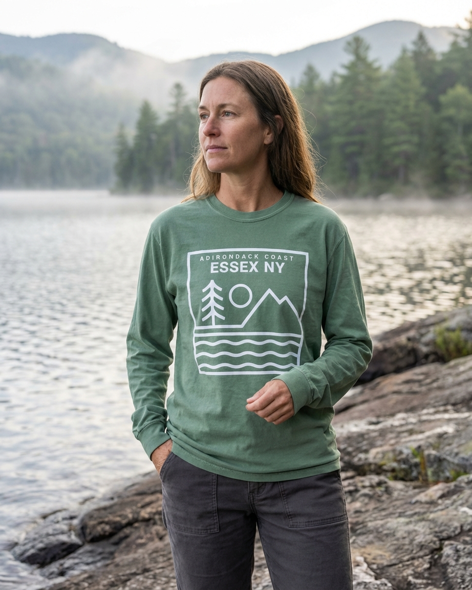 Person wearing a green sweatshirt with a nature-themed design by a lake and mountains.