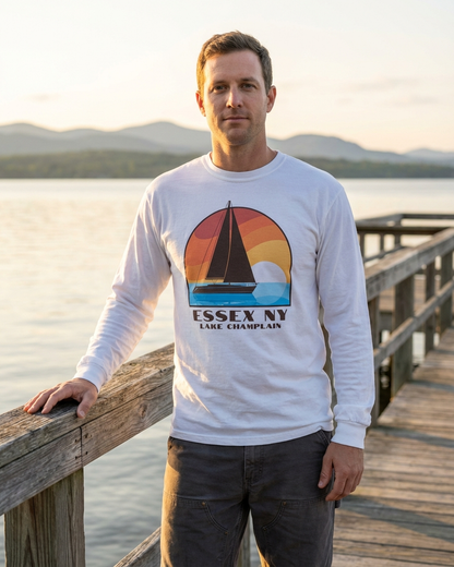 Man wearing a white sweatshirt with a sailboat design and text, standing on a wooden dock by a lake.