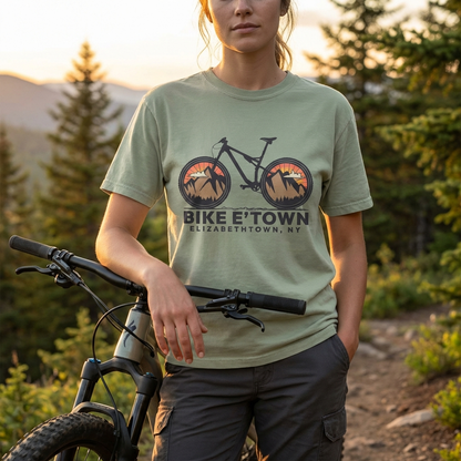 Person wearing a t-shirt with a bicycle graphic and text, standing outdoors with a bike.
