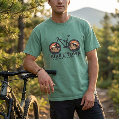 Man wearing a green t-shirt with a bicycle graphic and text, standing outdoors with a bike.