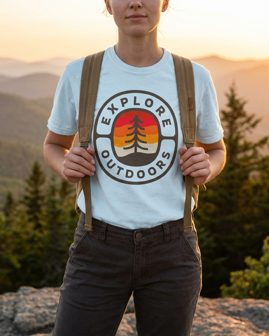 Person wearing a 'Explore Outdoors' t-shirt with a mountain and tree design, standing in a natural setting.