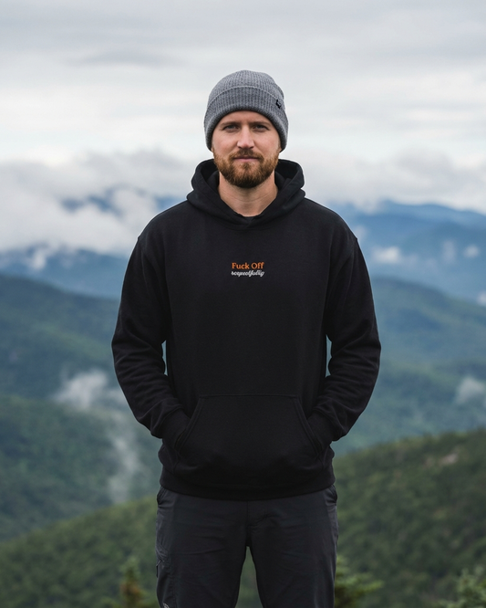 Man wearing a black hoodie with text in front of a mountainous landscape