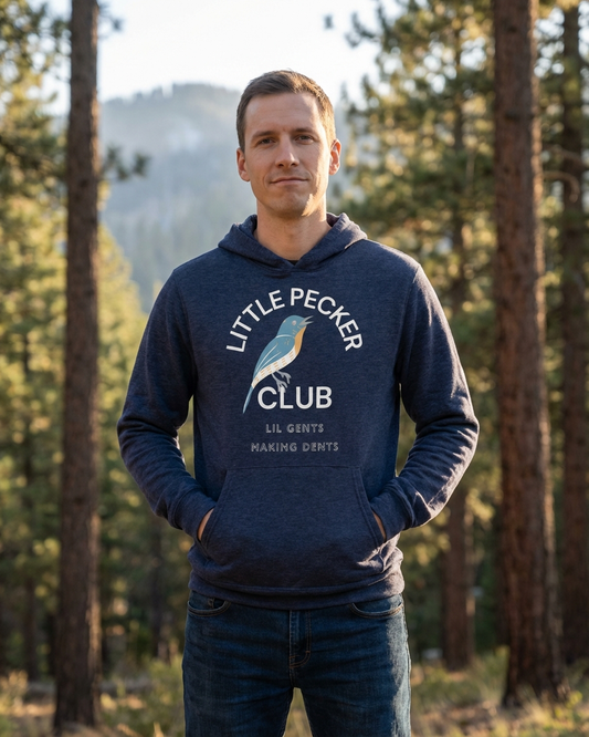 Man wearing a navy hoodie with 'Little Pecker Club' text and logo in a forest setting
