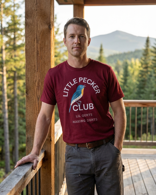Man wearing a 'Little Pecker Club' t-shirt on a wooden deck with a mountain view.