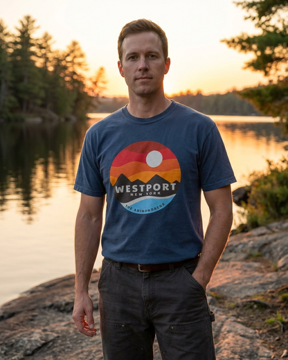 Man wearing a blue t-shirt with a 'Westport, New York' graphic standing by a lake at sunset.