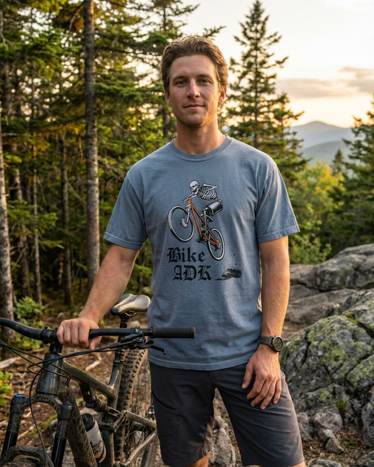 Man wearing a blue t-shirt with a bike graphic and text, standing outdoors with a mountain bike.
